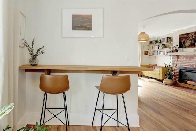 bar featuring light wood-type flooring, a fireplace, and arched walkways