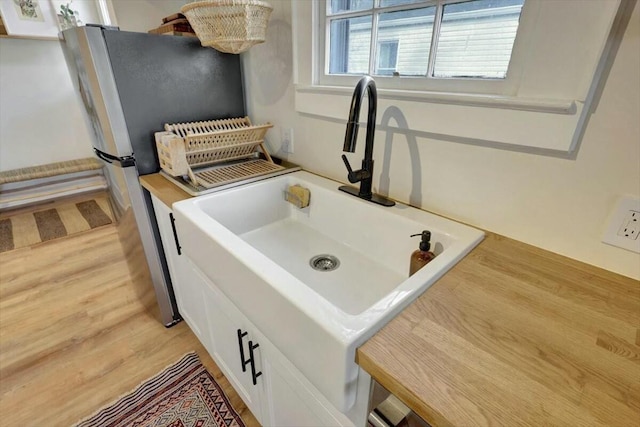 room details featuring light countertops, freestanding refrigerator, white cabinetry, a sink, and light wood-type flooring