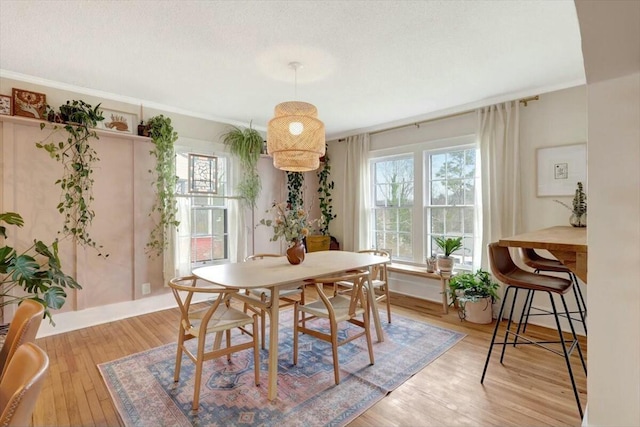 dining area with a textured ceiling, light wood-style floors, crown molding, and a healthy amount of sunlight