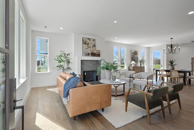 living room featuring wood finished floors, recessed lighting, an inviting chandelier, baseboards, and a tile fireplace