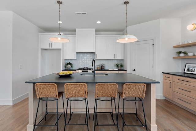 kitchen with visible vents, open shelves, a sink, light wood-style floors, and dark countertops