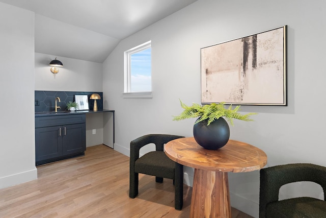 interior space with baseboards, light wood-type flooring, lofted ceiling, and a sink