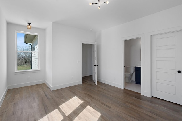 unfurnished bedroom featuring baseboards, wood finished floors, and ensuite bathroom