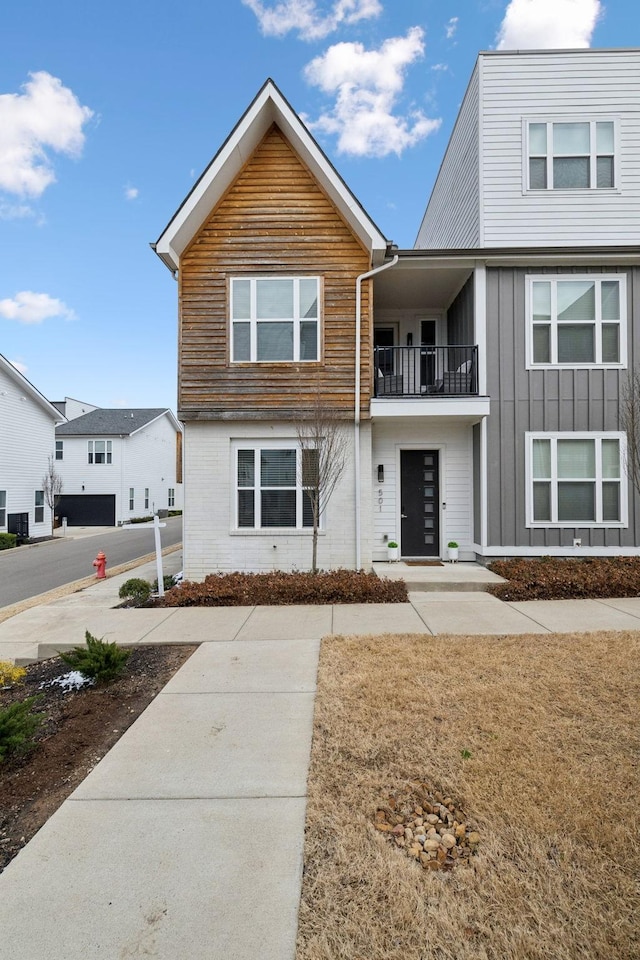 view of front of property featuring a balcony, board and batten siding, and brick siding