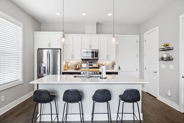 kitchen with pendant lighting, a center island with sink, light countertops, appliances with stainless steel finishes, and white cabinets