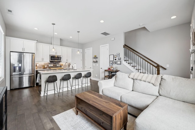 living room with stairs, dark wood-style flooring, visible vents, and recessed lighting