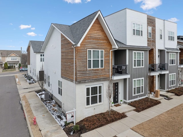 townhome / multi-family property with board and batten siding, a residential view, central AC, and roof with shingles