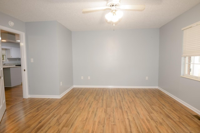 spare room with light wood-type flooring, a textured ceiling, and baseboards