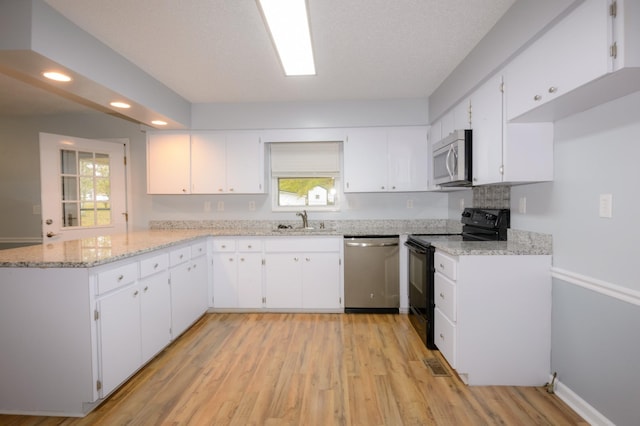 kitchen with light wood finished floors, appliances with stainless steel finishes, white cabinets, a sink, and a peninsula