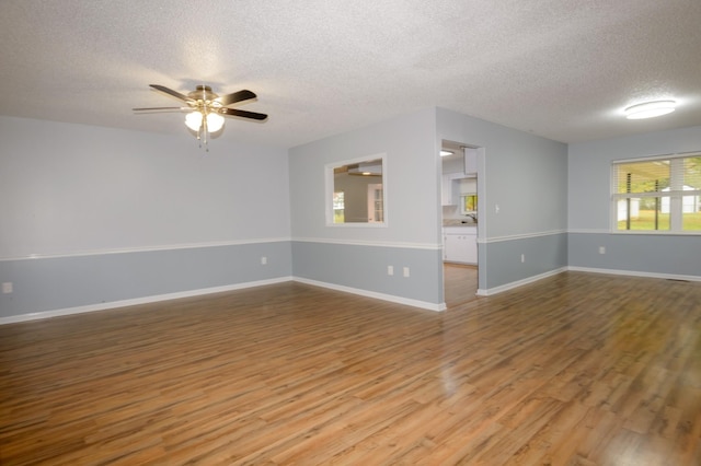 unfurnished room with a textured ceiling, wood finished floors, a ceiling fan, and baseboards