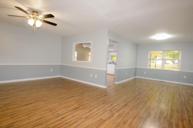 spare room with a ceiling fan, light wood-type flooring, a textured ceiling, and baseboards