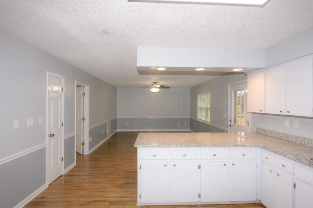 kitchen featuring open floor plan, white cabinets, a peninsula, and wood finished floors