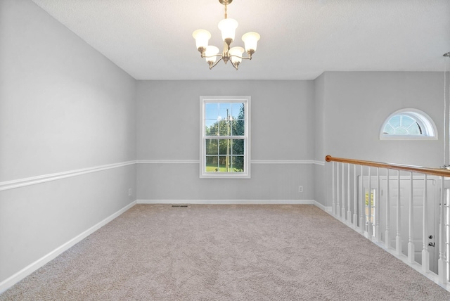 spare room featuring a textured ceiling, carpet flooring, visible vents, baseboards, and an inviting chandelier