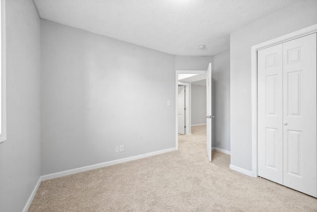 unfurnished bedroom featuring light carpet, a textured ceiling, a closet, and baseboards