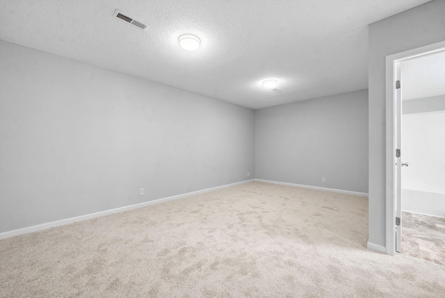 empty room with light carpet, a textured ceiling, visible vents, and baseboards