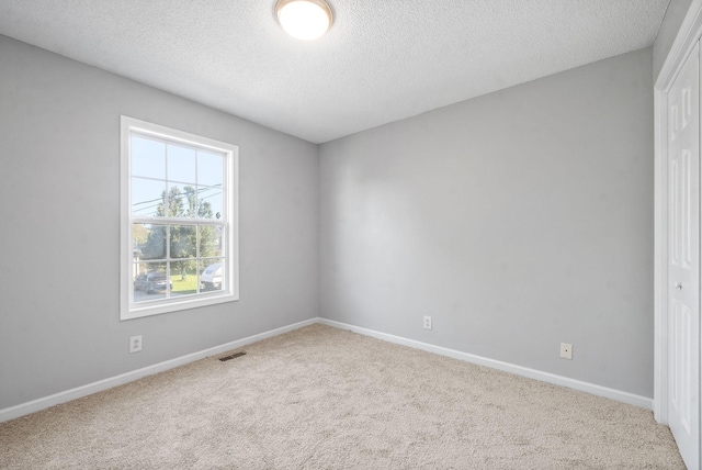 empty room featuring baseboards, a textured ceiling, visible vents, and light colored carpet