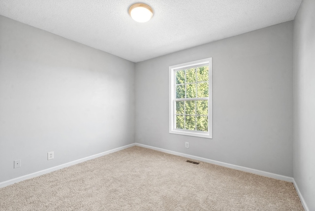 spare room featuring carpet floors, baseboards, visible vents, and a textured ceiling