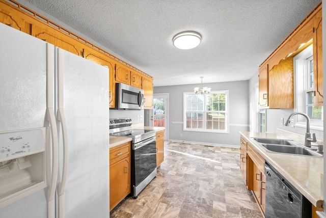 kitchen with appliances with stainless steel finishes, hanging light fixtures, an inviting chandelier, light countertops, and a sink