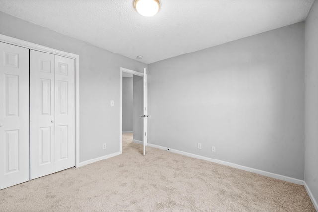 unfurnished bedroom featuring a closet, light carpet, a textured ceiling, and baseboards