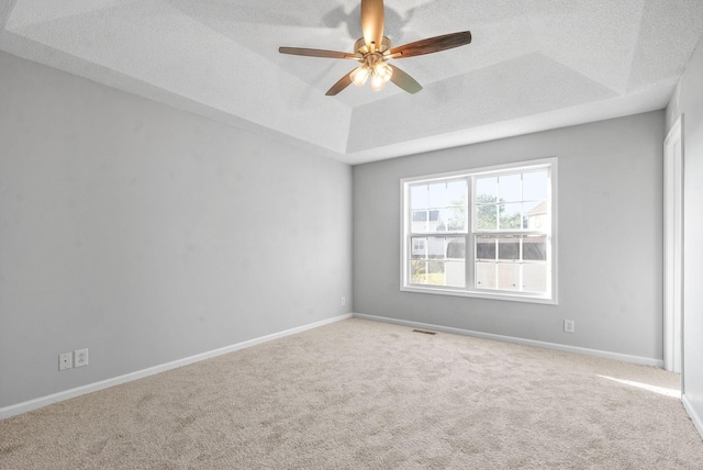 carpeted spare room featuring a textured ceiling, visible vents, a ceiling fan, baseboards, and a tray ceiling