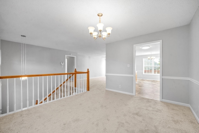 spare room featuring a chandelier, a textured ceiling, carpet flooring, and baseboards