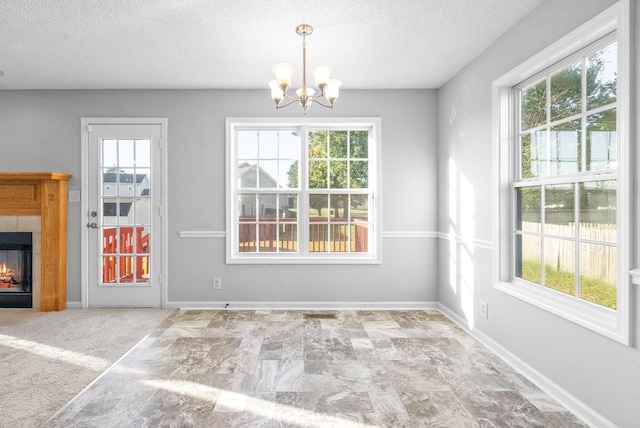 unfurnished dining area featuring a notable chandelier, a textured ceiling, baseboards, and a tiled fireplace