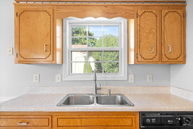 kitchen featuring brown cabinetry, light countertops, a sink, and dishwashing machine