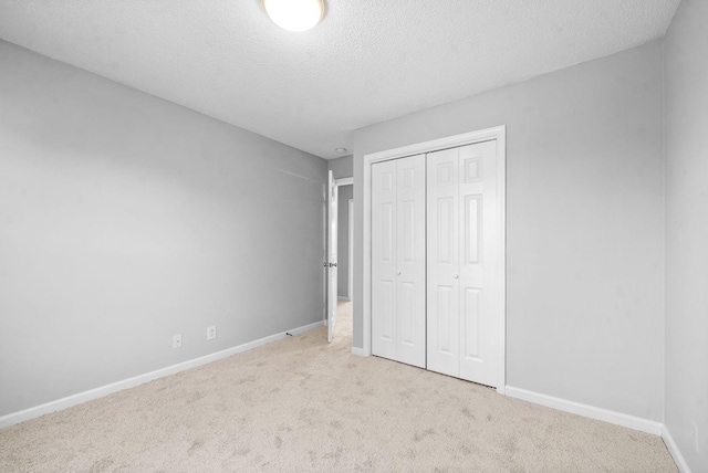 unfurnished bedroom with light carpet, a textured ceiling, baseboards, and a closet