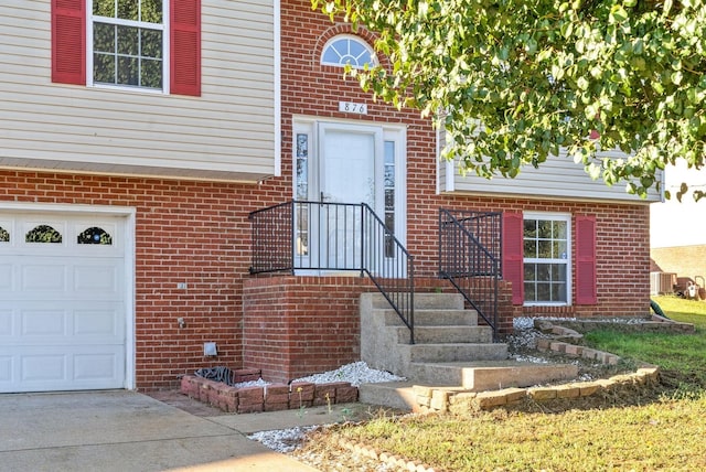 entrance to property with a garage, brick siding, driveway, and central AC unit