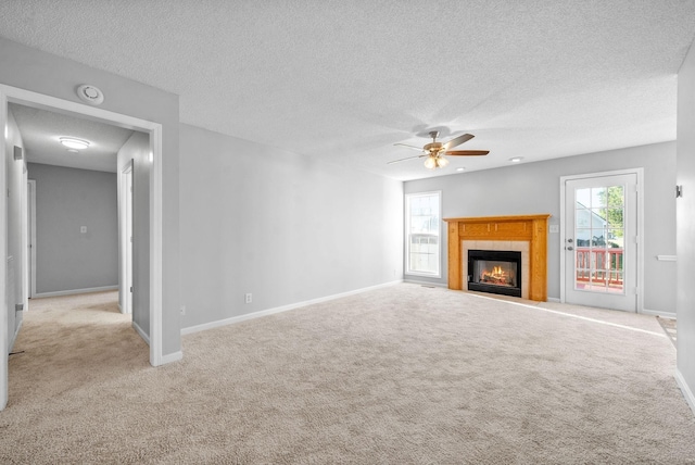 unfurnished living room with light colored carpet, a tiled fireplace, a ceiling fan, a textured ceiling, and baseboards