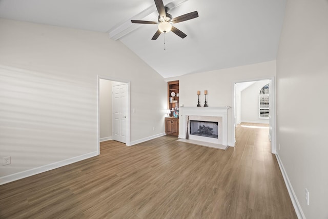 unfurnished living room featuring baseboards, a fireplace with flush hearth, ceiling fan, wood finished floors, and vaulted ceiling with beams