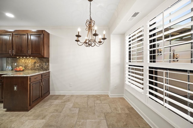 kitchen featuring baseboards, dark brown cabinets, decorative backsplash, stone tile flooring, and pendant lighting