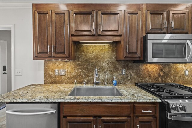 kitchen featuring decorative backsplash, light stone counters, stainless steel appliances, dark brown cabinets, and a sink