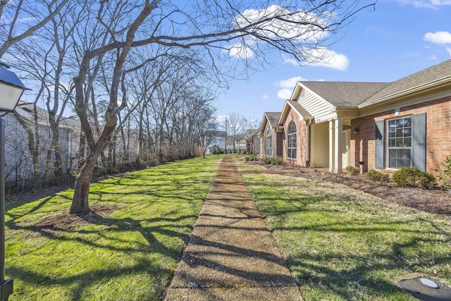 view of property exterior featuring a yard, roof with shingles, and brick siding