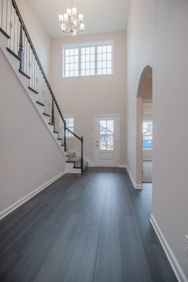 entrance foyer with dark wood-style floors, arched walkways, stairway, a high ceiling, and baseboards