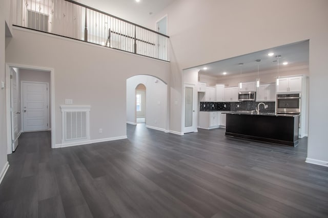 unfurnished living room featuring arched walkways, dark wood-style floors, visible vents, and baseboards