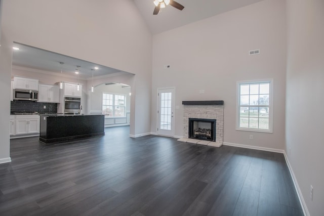 unfurnished living room featuring baseboards, visible vents, ceiling fan, dark wood-style flooring, and a stone fireplace