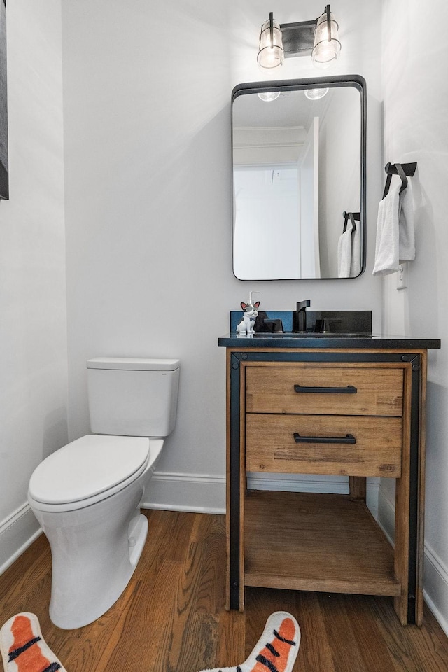 half bathroom with baseboards, vanity, toilet, and wood finished floors