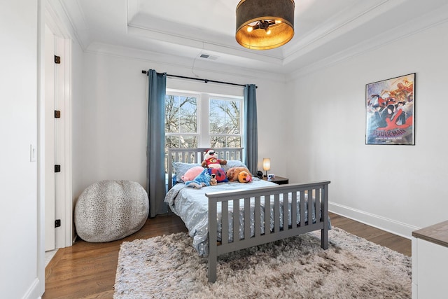 bedroom with baseboards, wood finished floors, a raised ceiling, and crown molding