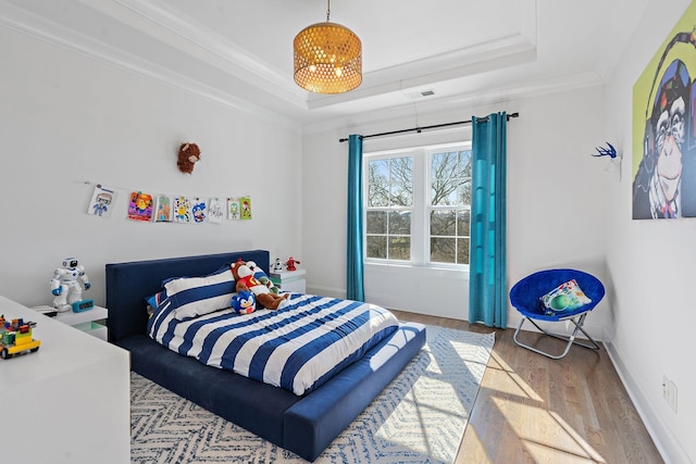 bedroom with crown molding, a tray ceiling, baseboards, and light wood-style floors