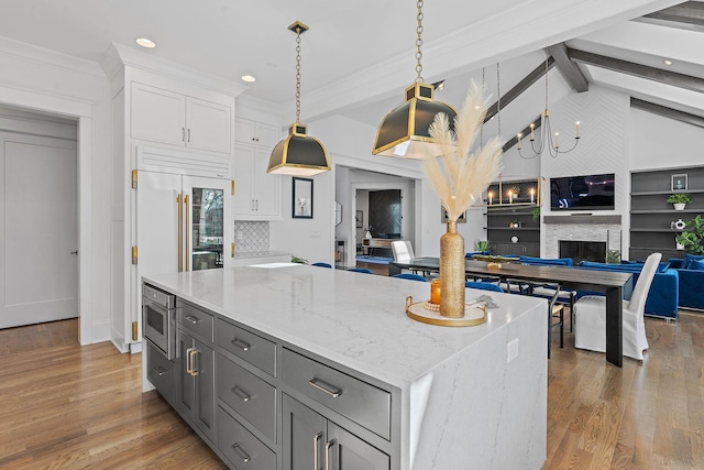 kitchen with a fireplace, open floor plan, white cabinetry, a kitchen island, and light stone countertops