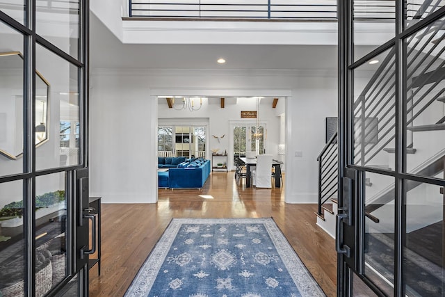 entrance foyer with a notable chandelier, wood finished floors, baseboards, stairs, and ornamental molding