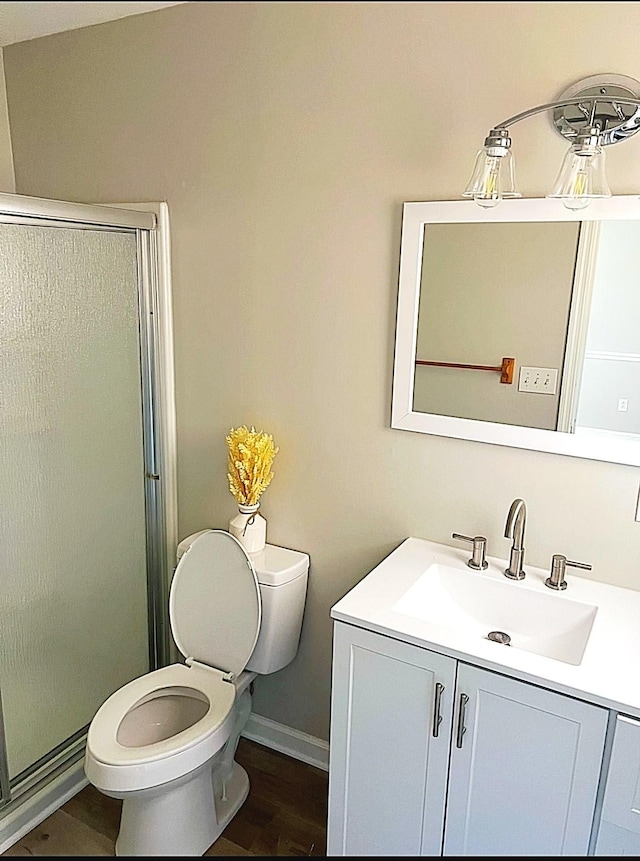 bathroom with toilet, a shower with shower door, wood finished floors, vanity, and baseboards