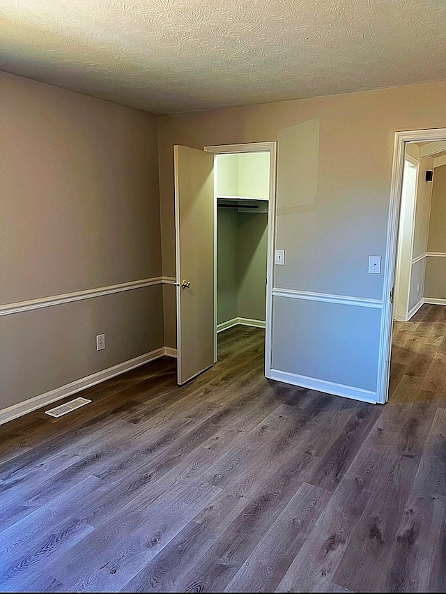 unfurnished bedroom featuring a walk in closet, visible vents, dark wood-type flooring, a textured ceiling, and baseboards