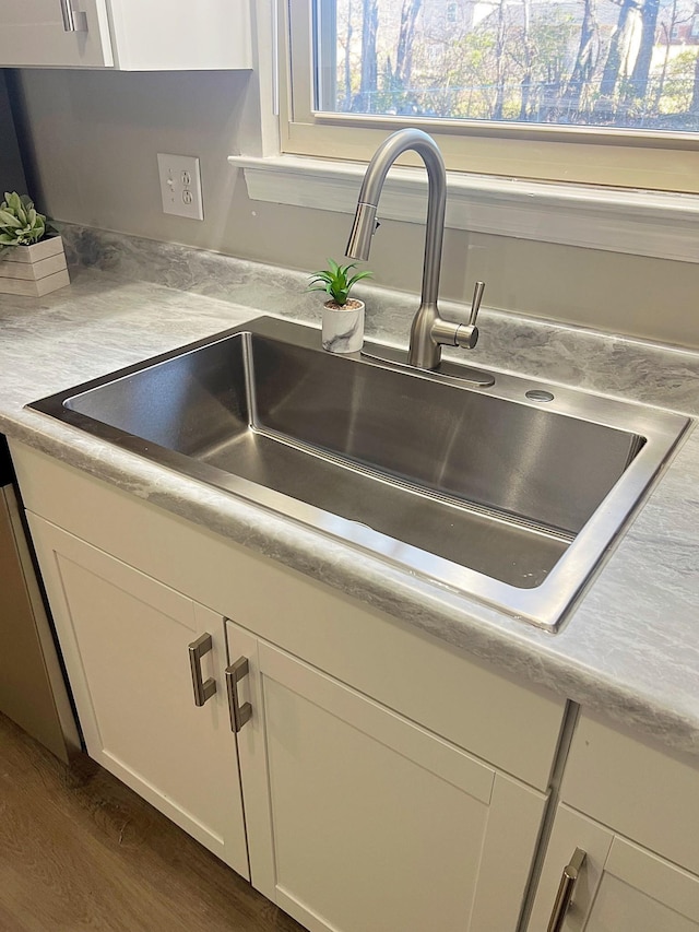 interior details with dark wood-type flooring, a sink, white cabinets, light countertops, and dishwasher