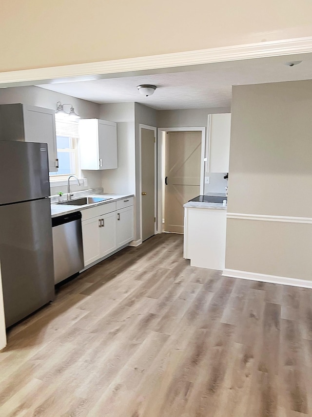 kitchen featuring stainless steel appliances, a sink, white cabinets, light countertops, and light wood-type flooring