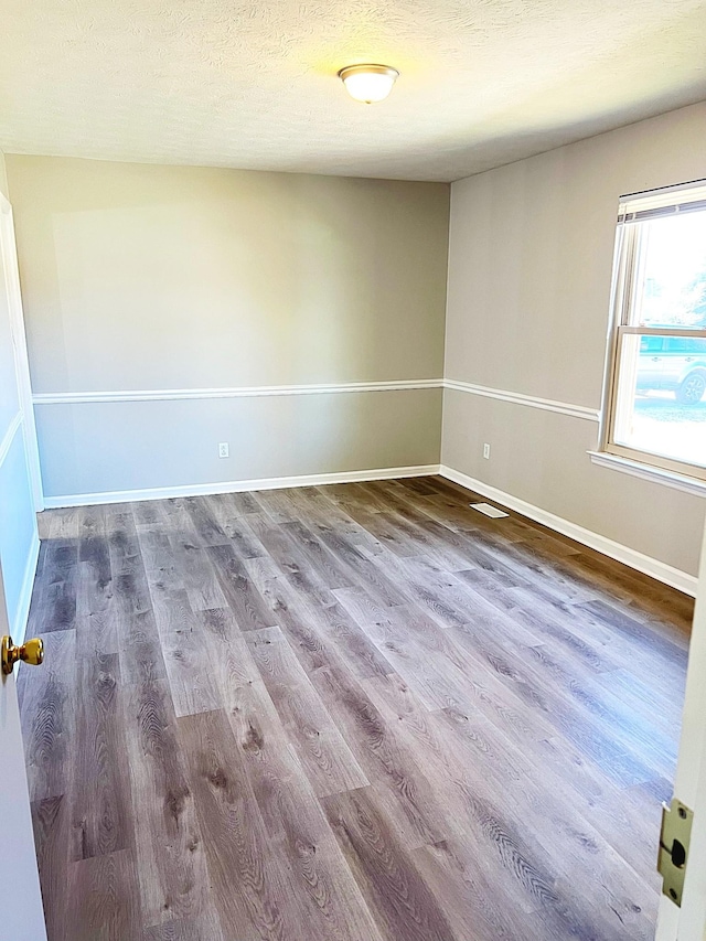 spare room featuring visible vents, a textured ceiling, baseboards, and wood finished floors