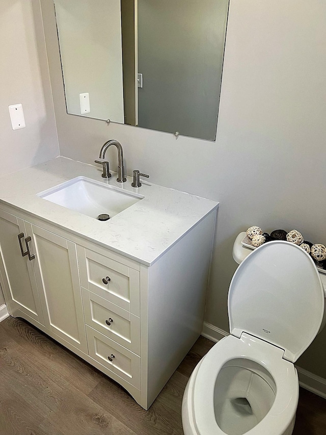 half bath featuring baseboards, vanity, toilet, and wood finished floors