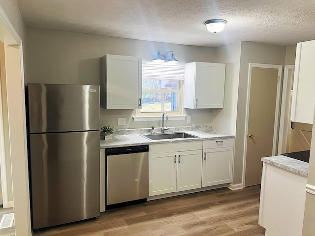 kitchen featuring appliances with stainless steel finishes, light wood-type flooring, a sink, and white cabinets