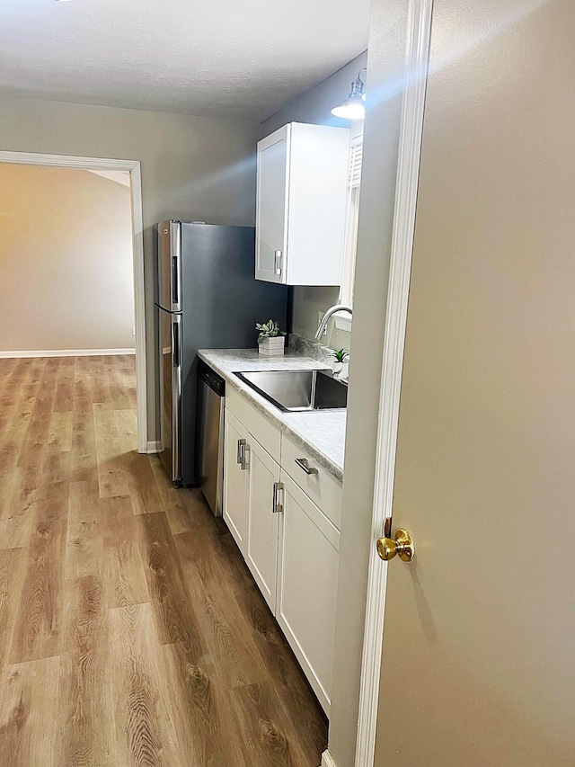 kitchen featuring light wood-type flooring, white cabinetry, a sink, and stainless steel dishwasher